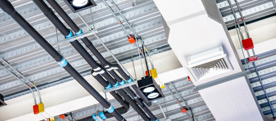 Electrical cable conduits wiring with colorful junction boxes, part of plumbing pipeline and ceiling air vent duct in modern building. Pipe and fitting for power, plumbing and air conditioning systems