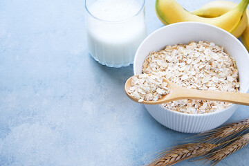 Oat flakes in bowl, milk and bananas on blue background