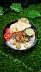 Soup or Soto Betawi with white coconut milk broth is a traditional Indonesian food typical of Jakarta. Served in a black bowl filled beef, potato, slices red tomatoes, lime, fried onions and crackers