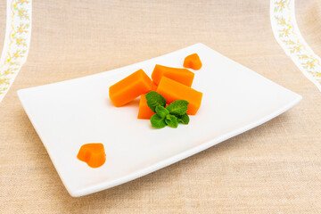 Freshly cut orange melon served on a sleek white plate with mint leaves
