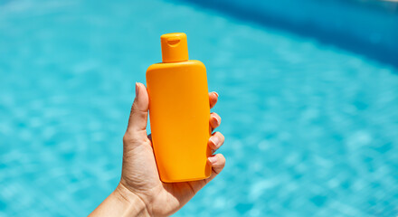 Woman holding sunscreen lotion by the swimming pool on sunny summer day