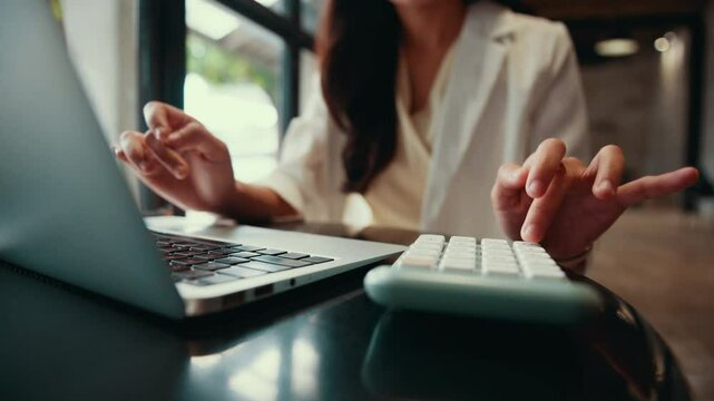 Professional businesswoman performing precise data entry and financial calculations, using laptop and calculator with focused concentration in modern office setting