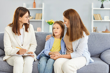 Young confident psychologist woman talking with worried upset little child girl patient sitting on...