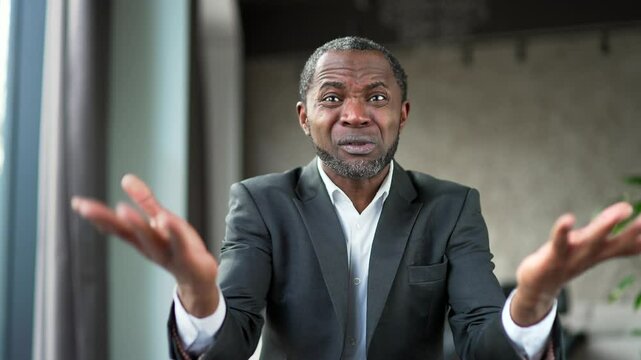 Webcam view. Angry dissatisfied african american businessman in suit arguing talking on video call looking at camera in business office. Excited boss emotionally talks shouts about problems. Close up