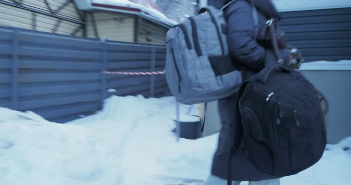Winter season. A young woman in winter clothes closes the car door and goes up the stairs of the house carrying two backpacks. Siberia.