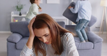 Tired upset unhappy stressed desperate mother does not know how to deal with hyperactive children who are having fun, jumping on sofa, fighting pillows and making noise. Parenting naughty kids concept - Powered by Adobe
