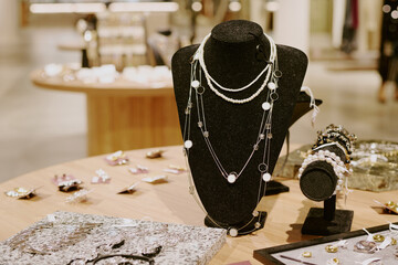 Medium close up of black velvet jewelry mannequin with adorable necklace and different types of accessories on wooden table