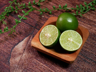 Closeup Fresh limes, consisting of one whole lime and two slices, neatly arranged on a small wooden plate. With brown background and decorative leaves enhance the natural.