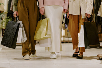Unrecognizable women dressed in fashionable clothes holding multicolored bags with brand new apparel