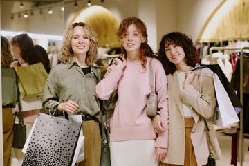 Portrait of attractive young adult shopaholics standing with paper bags full of female clothing in...