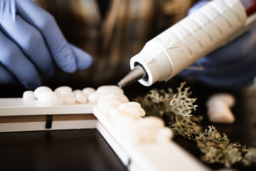 The process of decorating do it yourself. A woman works with wooden frame and white stones using a hot glue gun in her home workshop. Creating handmade interior decorations. Hobby. DIY.
