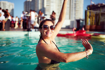 Naklejka premium Carefree woman dancing in a rooftop swimming pool during a party, enjoying the summer and the company of her friends