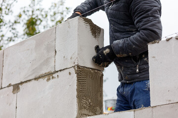A man is working on a brick wall, wearing a black jacket and gloves