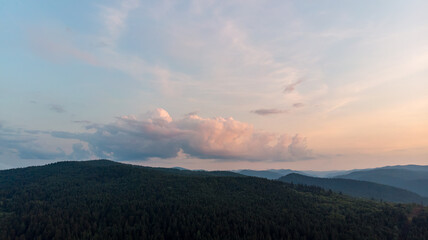 Majestic Mountains, Lush Green Forests, And Soft White Clouds On A Sunny Day. Aerial View Showcasing The Stunning Beauty Of Nature From A High Perspective.