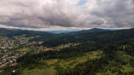 Naklejka premium Majestic Mountains, Lush Green Forests, And Dramatic Clouds With The Sun Casting A Golden Glow. Aerial View Capturing The Stunning Beauty Of Nature From A Bird’s-Eye Perspective. 