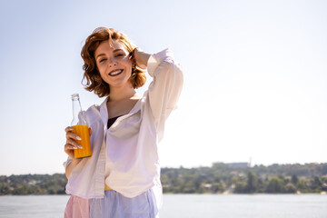 Portrait of young ginger woman posing at the camera at the beach while she drinks cocktail.