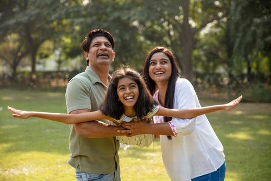 Indian happy father and mother holding daughter in hands while kid flying like plane, spreading hands, having fun. aspiration, parenthood and dream concept. Father swaying the daughter in hands.