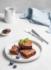 Chocolate brownie with nuts cut into pieces on a plate with blueberry and mint  on a light background