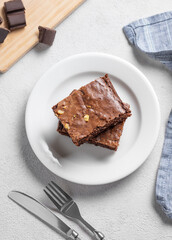 Chocolate brownie with nuts cut into pieces on a plate on a light background with fork and napkin.