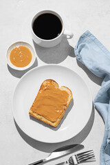 Peanut butter toast on a plate on a light background with a cup of freshly brewed coffee and shadow.