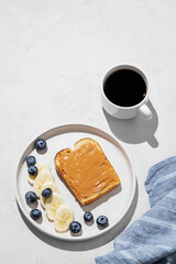 Peanut butter toast on a plate with banana and blueberry on a light background