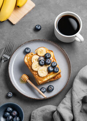 Peanut butter toast with banana, blueberry and honey on a plate on a dark  background