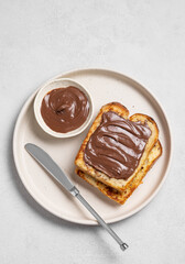 Toasted bread with chocolate cream on a plate on a light  background with knife.
