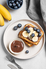 Toasted bread with chocolate cream, blueberries and banana on a plate on a light background