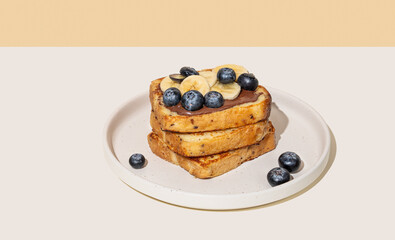Toasted bread with chocolate cream, blueberries and banana on a plate on a light background