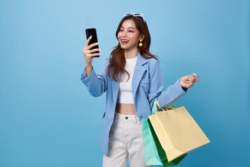 Beautiful Asian woman carrying shopping bags and using mobile phone in hands shopping online...