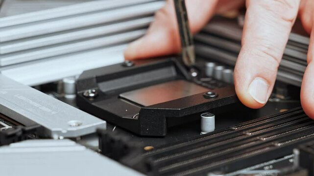 The master tightens the screws to attach the backplate to the motherboard. PC assembly. Installing a liquid cooling system for the processor.