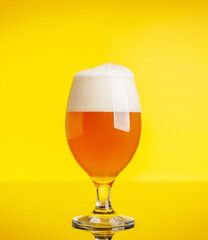 A frothy glass of fresh beer against a bright yellow background