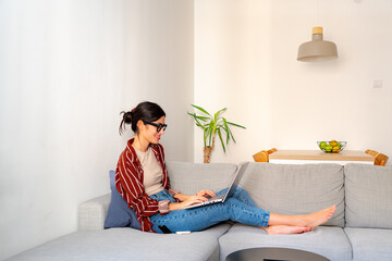 Peaceful home setting. A young woman smiling while working on her laptop in a well-lit living room. Minimalist and lifestyle concept
