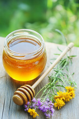 Honey jar with wooden dipper and wildflowers in daylight