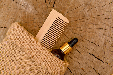 Cosmetic oil and wooden comb in canvas bag on wooden background.