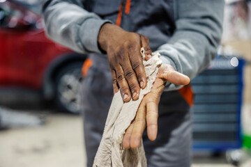Close up of interracial mechanic cleaning greasy dirty hands with an old rag at car service.
