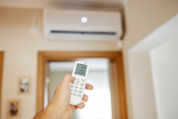 Close up of hand holding remote control and increasing temperature of air conditioner.