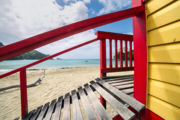 Bright red and yellow wooden lifeguard shack at Bloody Bay, overlooking a sandy beach and tcrystal...