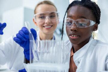 Medical woman and her colleague in laboratory using pipette conducting experiment on samples