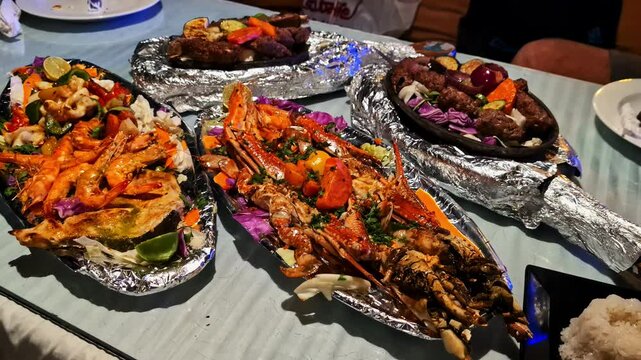 A vibrant seafood and barbecue platter with shrimp, lobster, kebabs, and colorful garnish