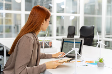 Ginger young woman working in the office on a new project of wind farm
