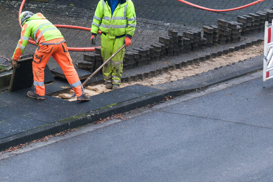 Konzept Glasfaserausbau, Internet, Kommunikation und: Arbeiter bei Bauma&szlig;nahmen f&uuml;r die Verlegung von Glasfaserleitungen f&uuml;r den Hausanschluss in einer Stra&szlig;e
