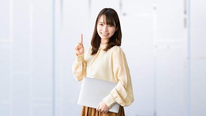 パソコンを持って案内をする笑顔の女性・ビジネスウーマン