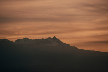 Landscape of the Nevado de Toluca at sunset, with snow, clouds and a sky with ochre and red colors can be seen.