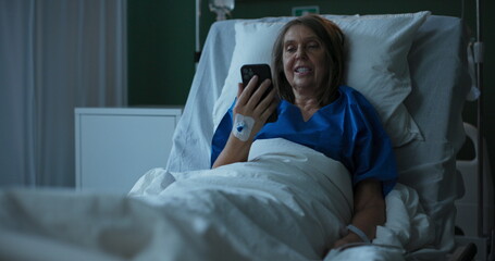 Naklejka premium Elderly lady in hospital, talking on phone through video, brightening her day.