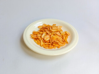 Fried garlic chips or slice on white plate. Use as condiment topping in various Indonesian culinary meal.