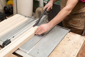 The carpenter saws the board, holding it with a special stop