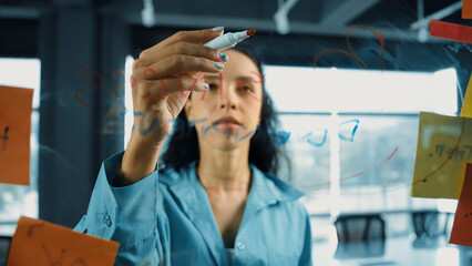 Portrait of smart professional hispanic businesswoman writes marketing ideas on glass board with...