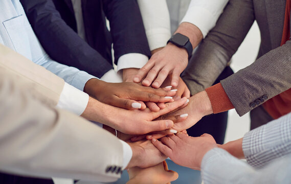 Corporate teamwork and unity. Gesture with folded hands that symbolizes unity, diversity and cooperation in corporate world. Close up of folded hands of business colleagues of different ethnic groups. - Powered by Adobe
