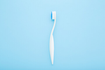 New white toothbrush with soft bristles on light blue table background. Pastel color. Closeup. Top down view.